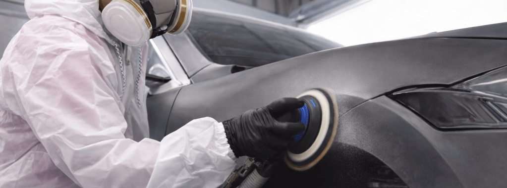 Technician polishing the surface of a car in an automotive repair workshop.