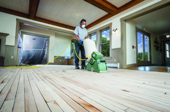 Man wearing PPE refinishing a hardwood floor