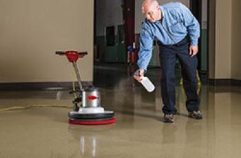 Man spraying a floor next to a buffing machine
