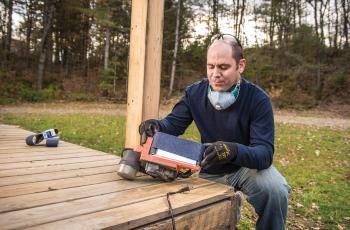 Man applying abrasive belt to a belt sander on a deck
