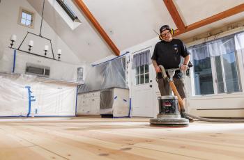 Man sanding wood floors using Norton SandDollar floor pads on a rotary floor buffer