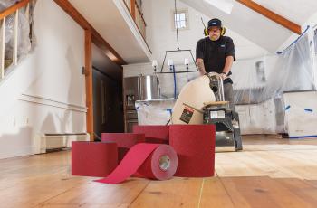 Man using a belt sander to sand a wood floor with Norton Red Heat shown in the foreground
