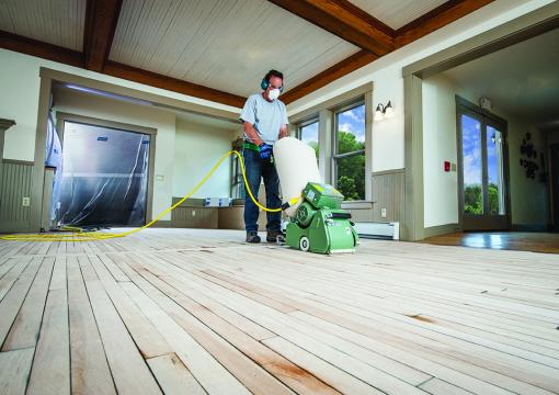 Man wearing PPE refinishing a hardwood floor