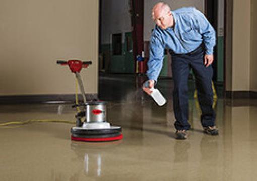 Man spraying a floor next to a buffing machine