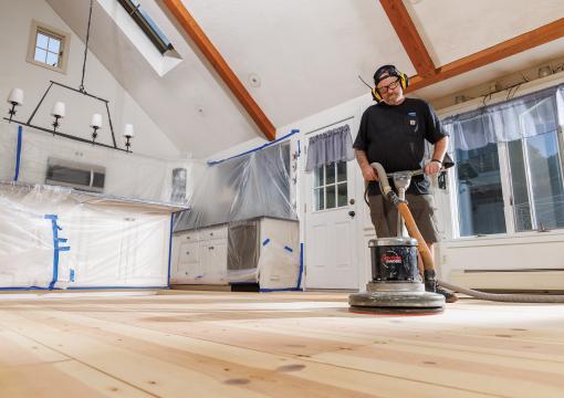 Man sanding wood floors using Norton SandDollar floor pads on a rotary floor buffer