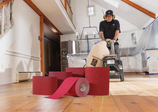 Man using a belt sander to sand a wood floor with Norton Red Heat shown in the foreground