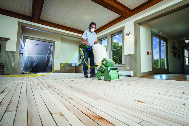 Man wearing PPE refinishing a hardwood floor