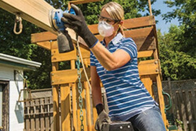 Woman sanding a play structure using a power tool