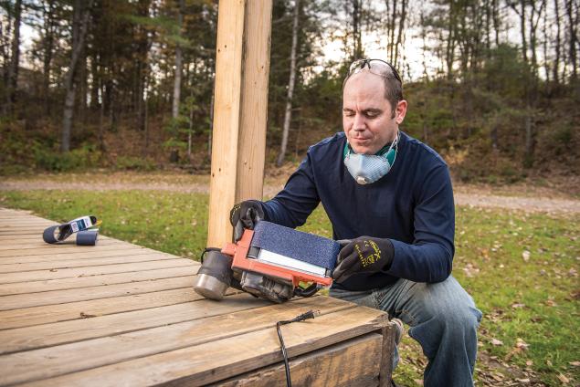 Man applying abrasive belt to a belt sander on a deck
