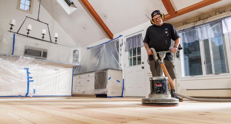 Man sanding wood floors using Norton SandDollar floor pads on a rotary floor buffer
