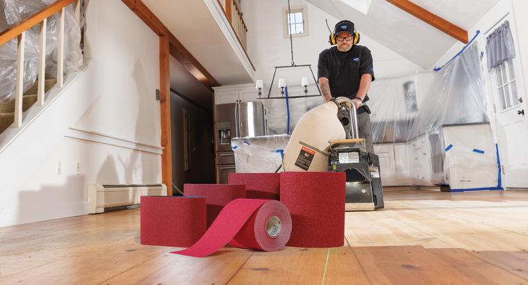 Man using a belt sander to sand a wood floor with Norton Red Heat shown in the foreground